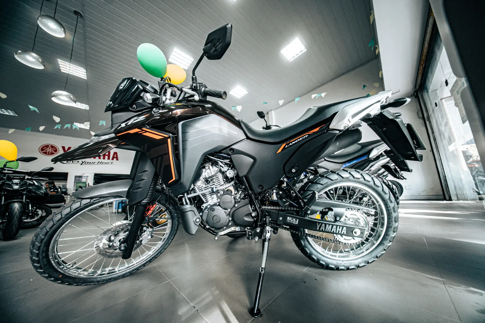 Lander 250 preta e cinza com detalhes laranja, vista de lado no salão da loja.