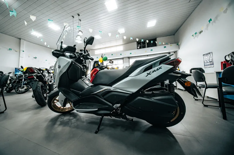XMAX 250 cinza com rodas douradas, vista de lado no salão da loja.